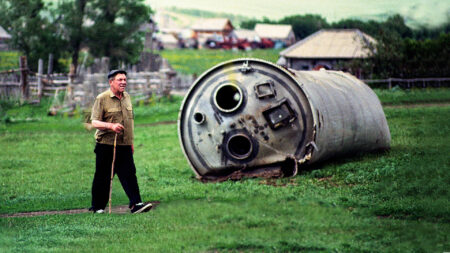 Old man walking past rocket debris in a field
