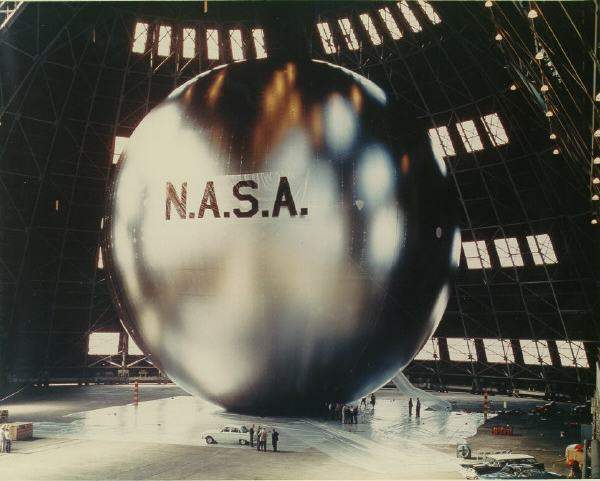 A giant metallic balloon satellite inflated in a hangar