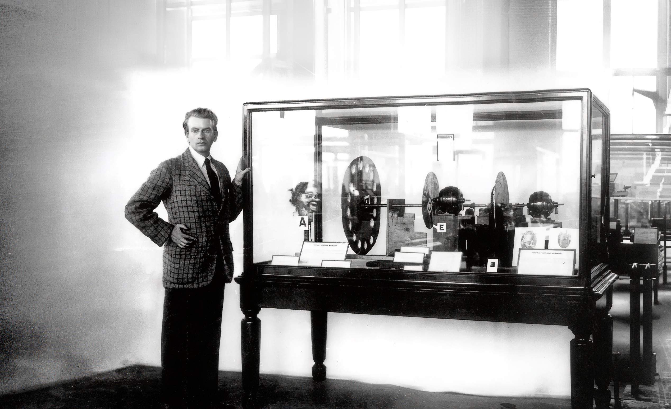 Old picture of John Logie Baird standing next to his first mechanical TV prototype